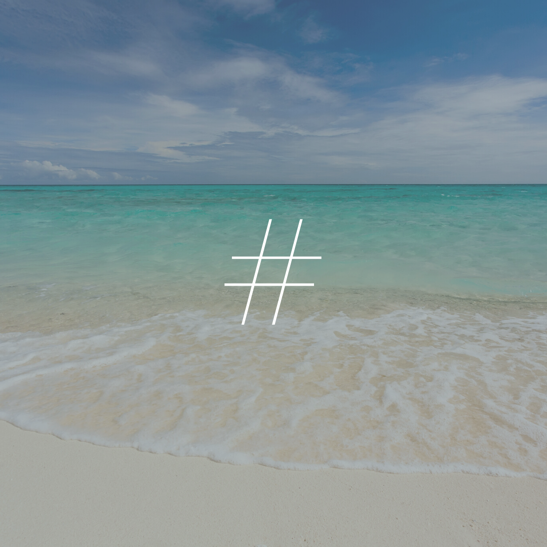 The bright greenish blue ocean laps the shore of the beach behind a white hashtag symbol.